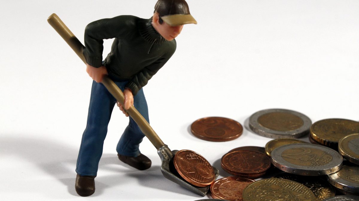 A imagem mostra uma pessoa juntando moedas gigantes com uma pá