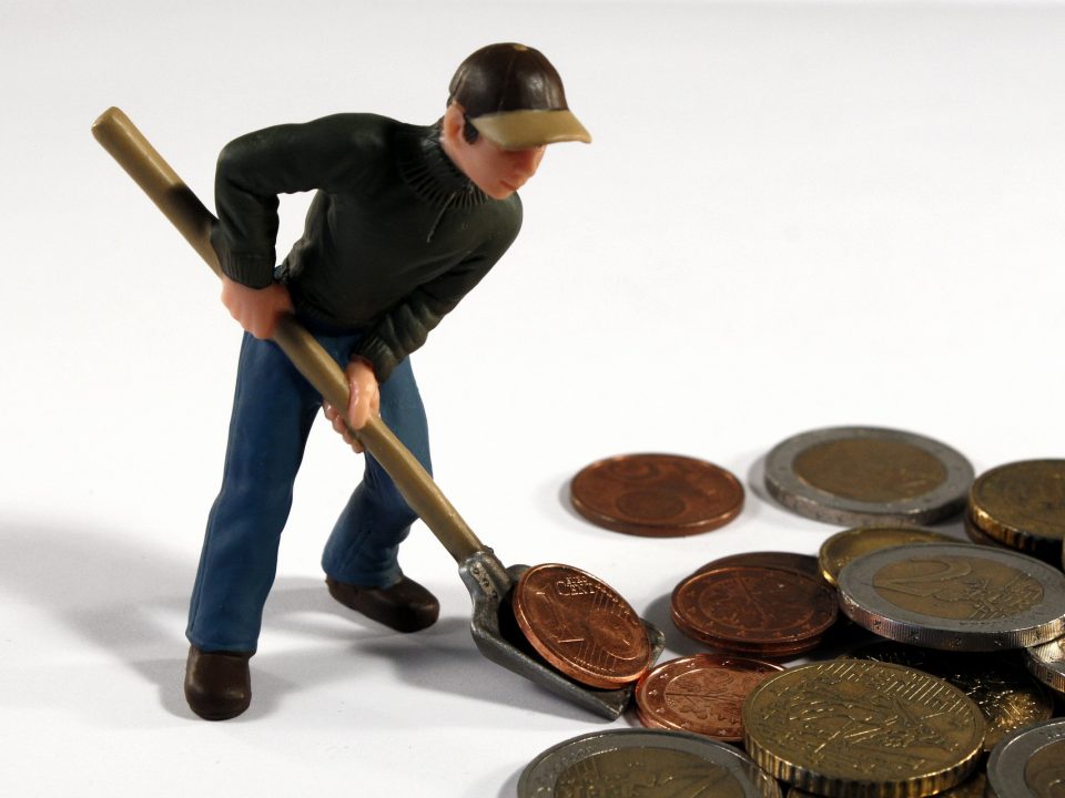 A imagem mostra uma pessoa juntando moedas gigantes com uma pá